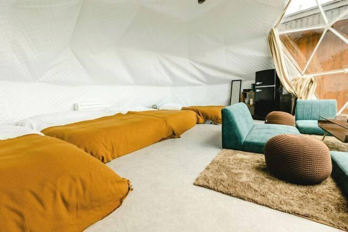 A tent-style room with a bed, sofa, ottoman, and a geometric window design.