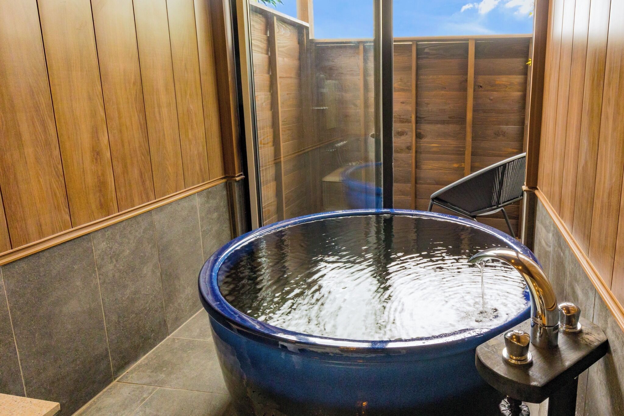 A bathroom with a large blue bathtub, wooden walls, and a glass shower enclosure.