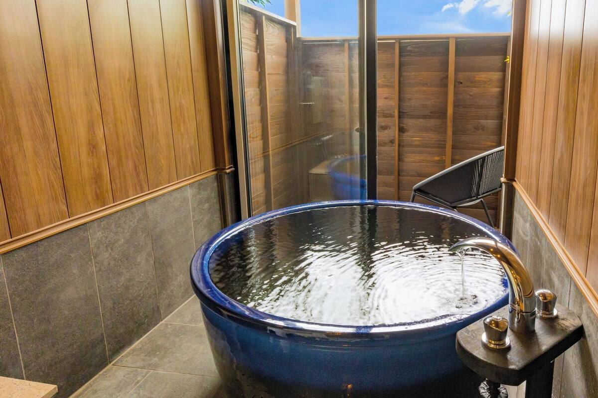 A bathroom with a large blue bathtub, wooden walls, and a glass shower enclosure.