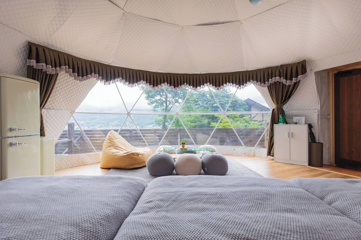 A cozy room with a bed, a bean bag, and a view of the outdoors through a large window.