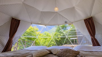 Habitación tipo tienda de campaña con cama, cortinas y vistas a árboles.