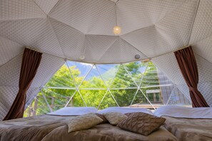 Habitación tipo tienda de campaña con cama, cortinas y vistas a árboles.