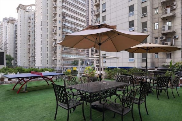 Un espacio al aire libre con mesas, sillas y una mesa de ping pong, además de sombrillas.