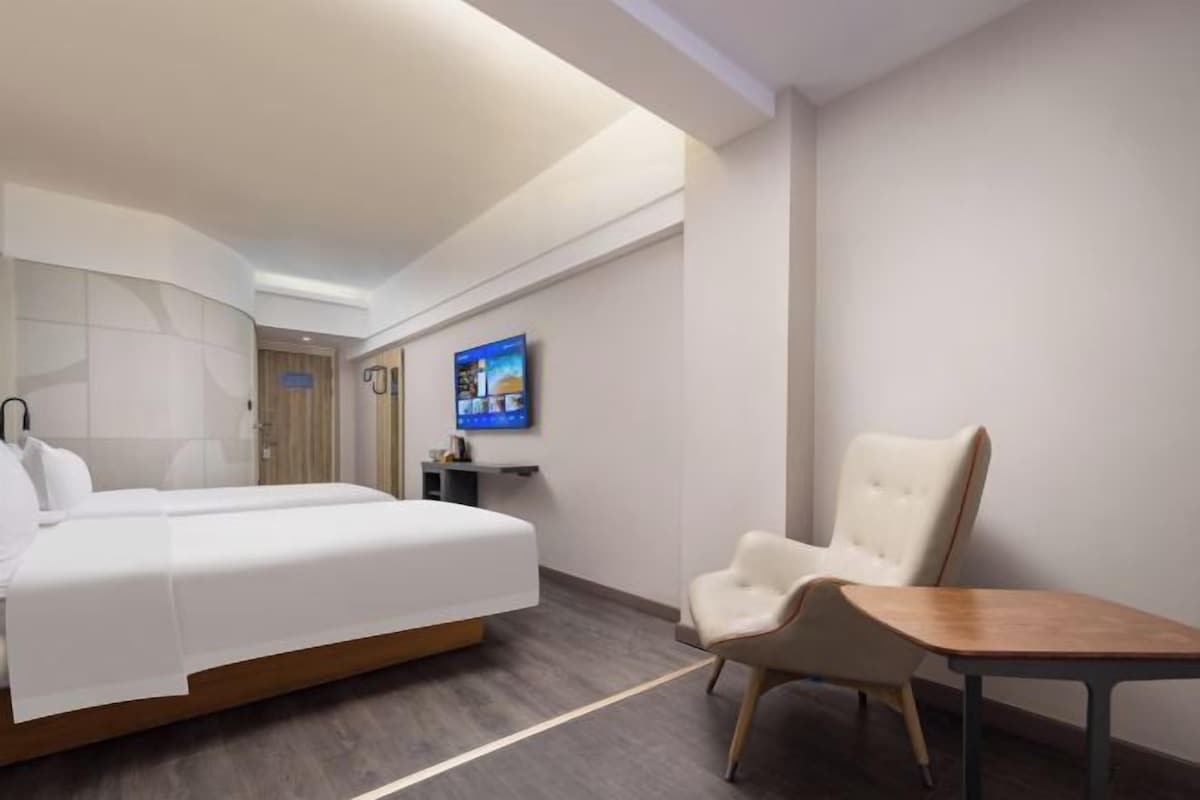 A hotel room with a bed, a TV, a chair, and a small table.