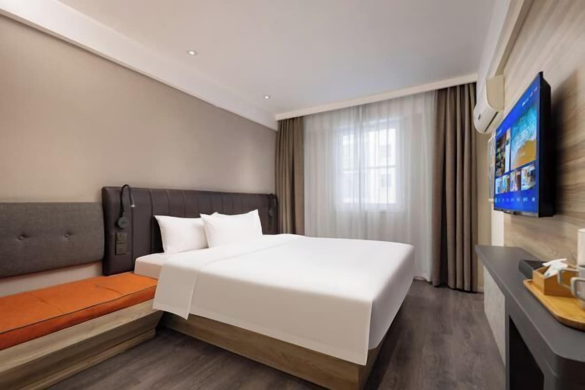 A hotel room with a large bed, a sofa bed, a flat-screen TV mounted on the wall, and a window with curtains.