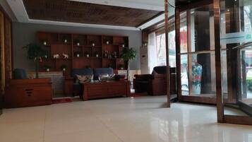 A spacious lobby with a wooden reception desk, a seating area with sofas, and a large glass door leading outside.