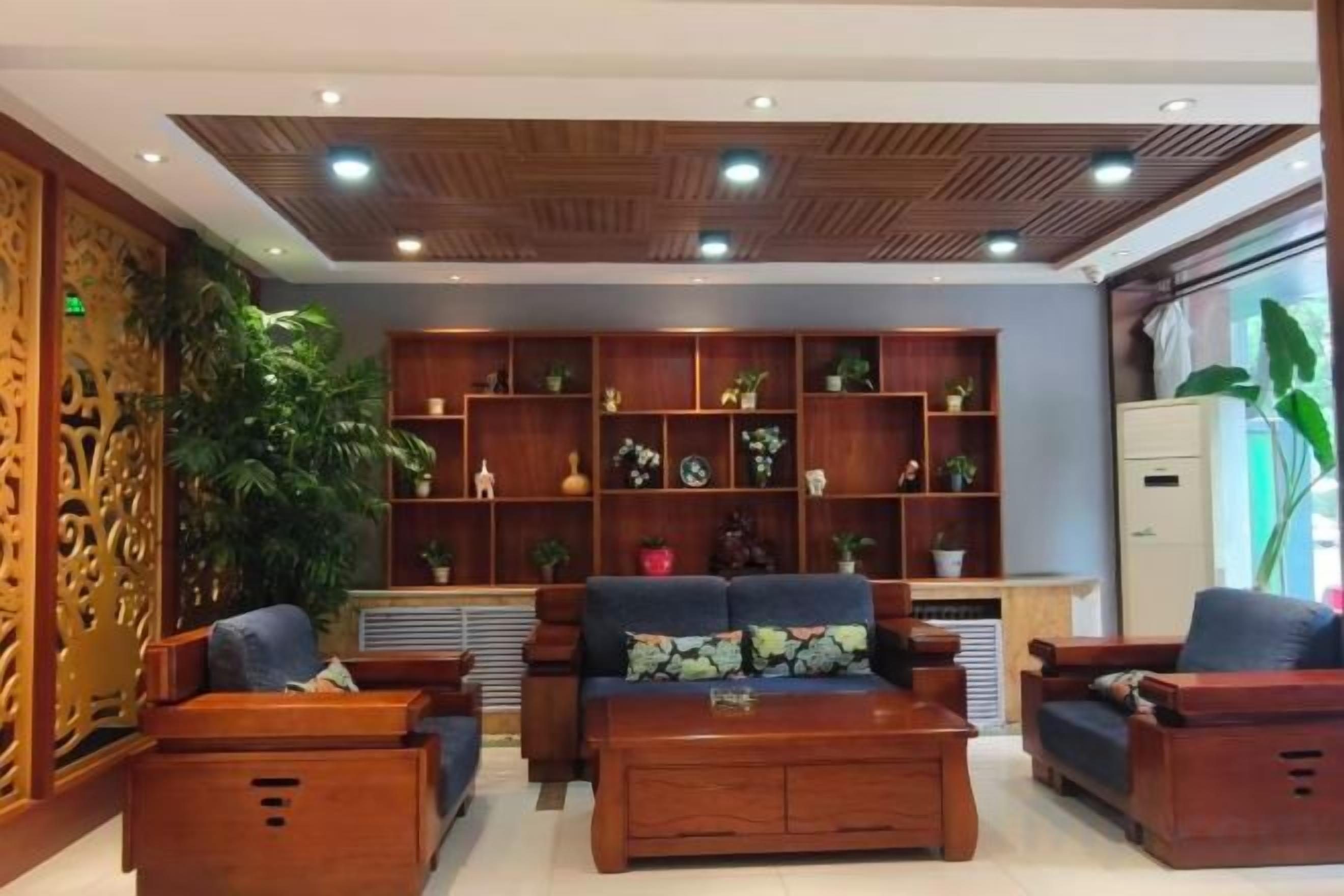 A lobby with wooden furniture, a large plant, and a bookshelf.