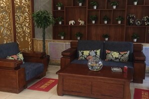 Ein Wohnzimmer mit einer Couch, zwei Sesseln, einem Couchtisch und einem Bücherregal mit Blumentöpfen.