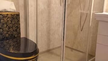 A corner of a bathroom with a glass shower enclosure and a black toilet with gold trim.