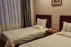 Een hotelkamer met twee eenpersoonsbedden, een nachtkastje van hout met een telefoon en een raam met gordijnen.