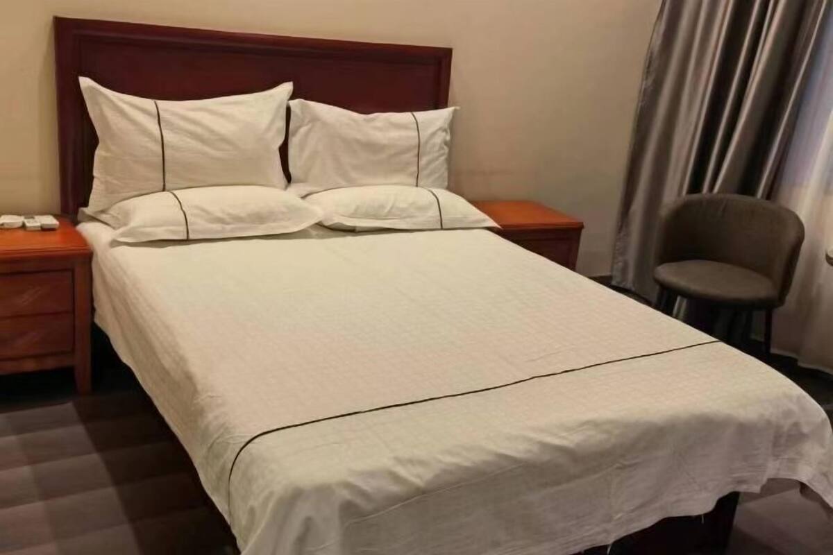 Een hotelkamer met een enkel bed, een houten hoofdbord, een nachtkastje met telefoon en een stoel.