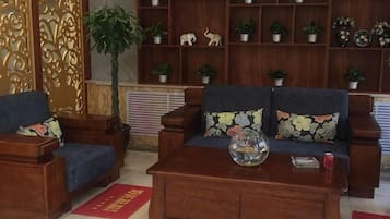 A living room with a sofa, two armchairs, a coffee table, and a bookshelf filled with plants.