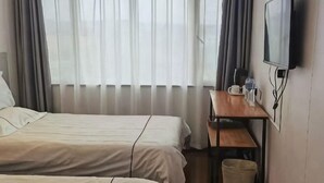 Ein Hotelzimmer mit zwei Betten, einem Schreibtisch mit Stuhl, einem Fernseher und einem Fenster mit Vorhängen.