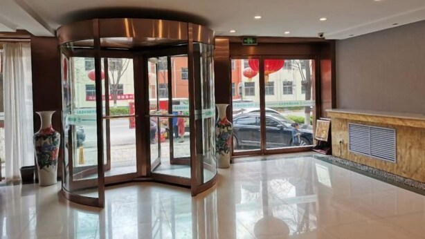 Eine Hotellobby mit einer sich drehenden Tür, einem Empfangsbereich und großen Fenstern mit Blick auf die Straße.