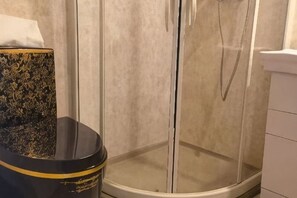 Een douchecabine met glazen wanden, een witte betegelde muur en een zwart toilet met gouden accenten.
