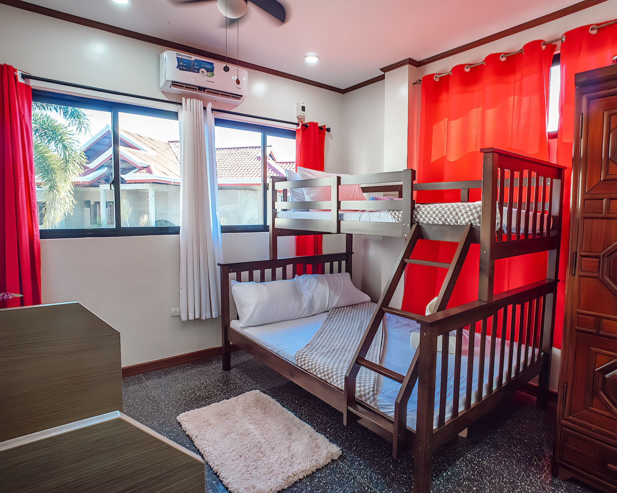 A bunk bed room with a window, red curtains, a white air conditioner, and a wooden door.