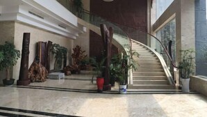 Un hall d’entrée spacieux, doté d’un sol en marbre, d’un escalier en colimaçon et de différents pots de plantes.