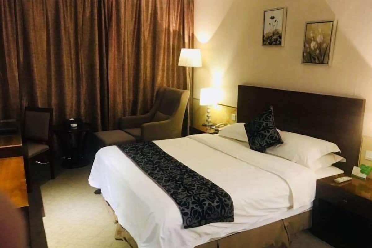 Une chambre d’hôtel avec un lit, une chaise, une table de chevet, une lampe et un rideau.