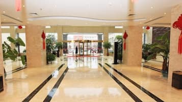 A spacious lobby with a marble floor, a central entrance, and potted plants.