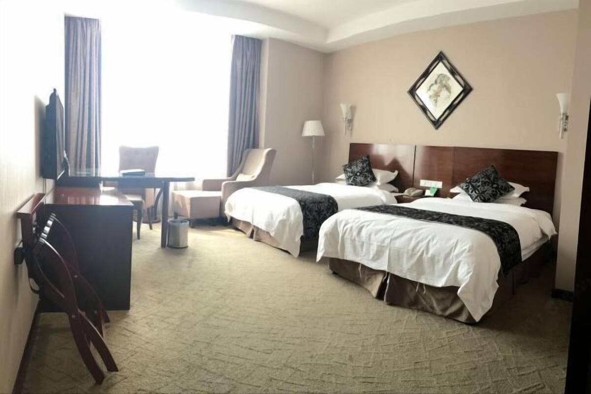 Une chambre d’hôtel avec deux lits, un bureau, une chaise, une télévision et une lampe.