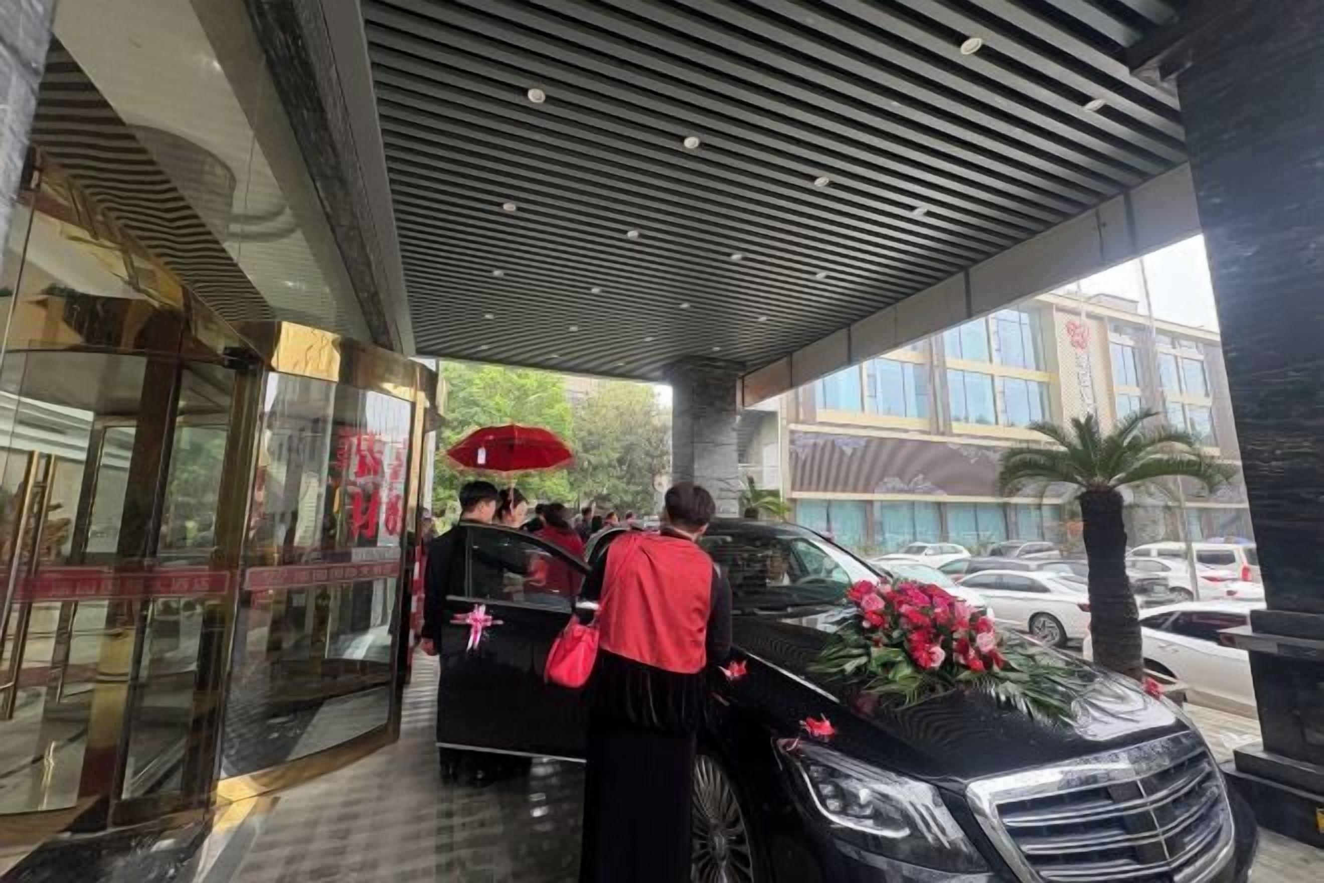 A hotel entrance with a covered walkway, a glass door entrance, and a black car with flowers.