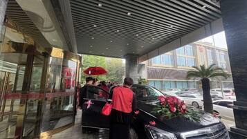 A hotel entrance with a covered walkway, a glass door entrance, and a black car with flowers.
