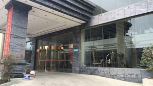 Une entrée moderne avec une porte en verre, une façade en marbre et une enseigne rouge sur le côté gauche.