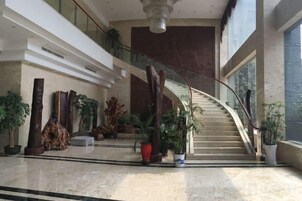 Un vestíbulo amplio con una escalera curva, plantas en macetas y una gran lámpara de araña.