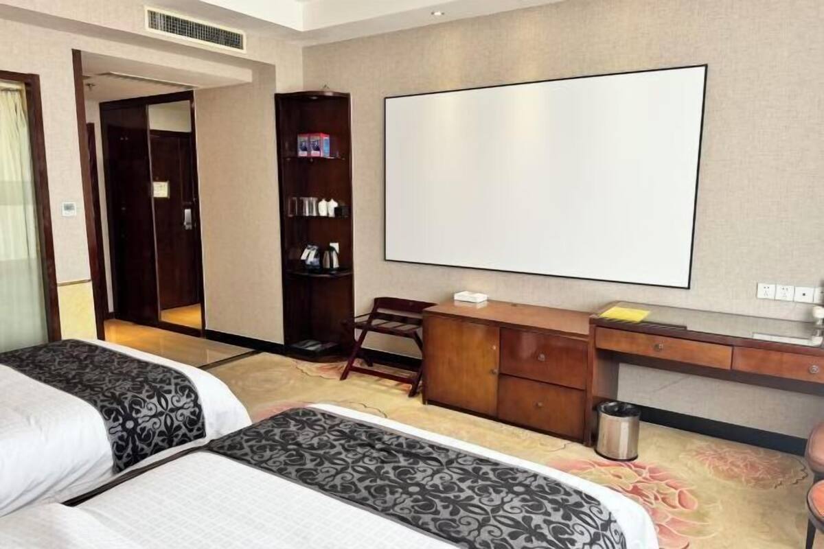 Une chambre d’hôtel avec deux lits, un bureau, une bibliothèque, un grand miroir et un tableau blanc.