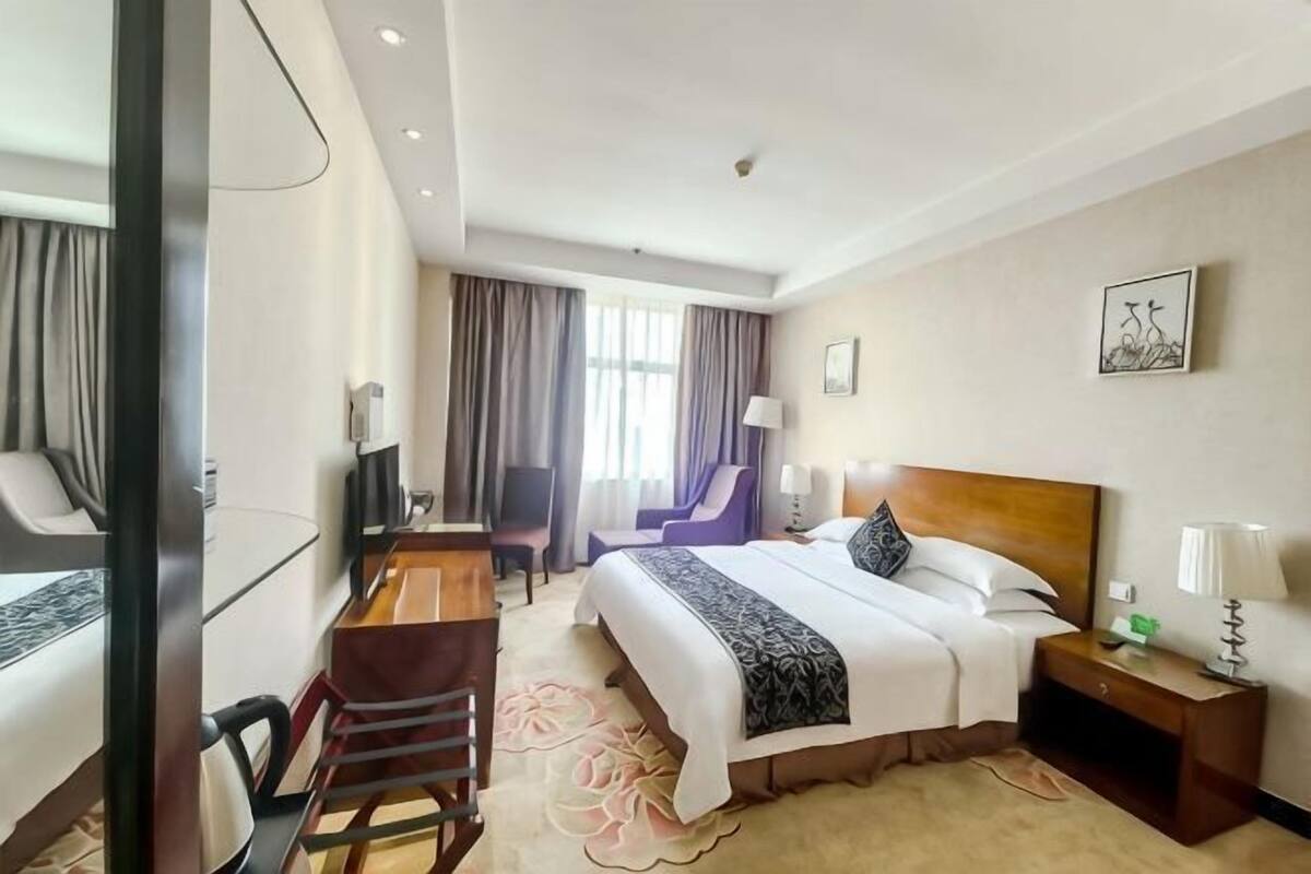 Une chambre d’hôtel avec un lit, un bureau, une chaise, une télévision et une fenêtre avec des rideaux.