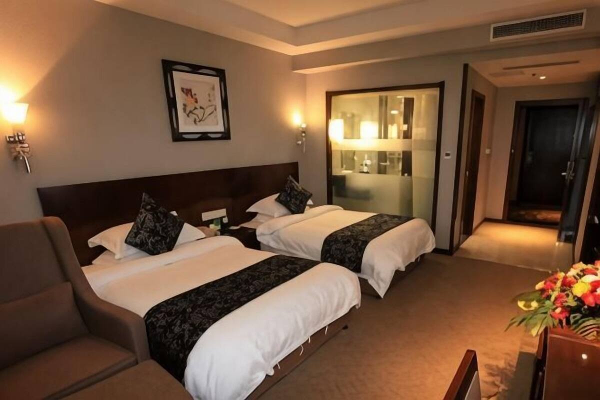 Une chambre d’hôtel avec deux lits, une chaise, un bureau, un miroir et une porte donnant sur une salle de bain.