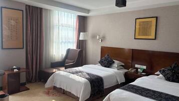 A hotel room with two beds, a desk, a chair, and a window with curtains.