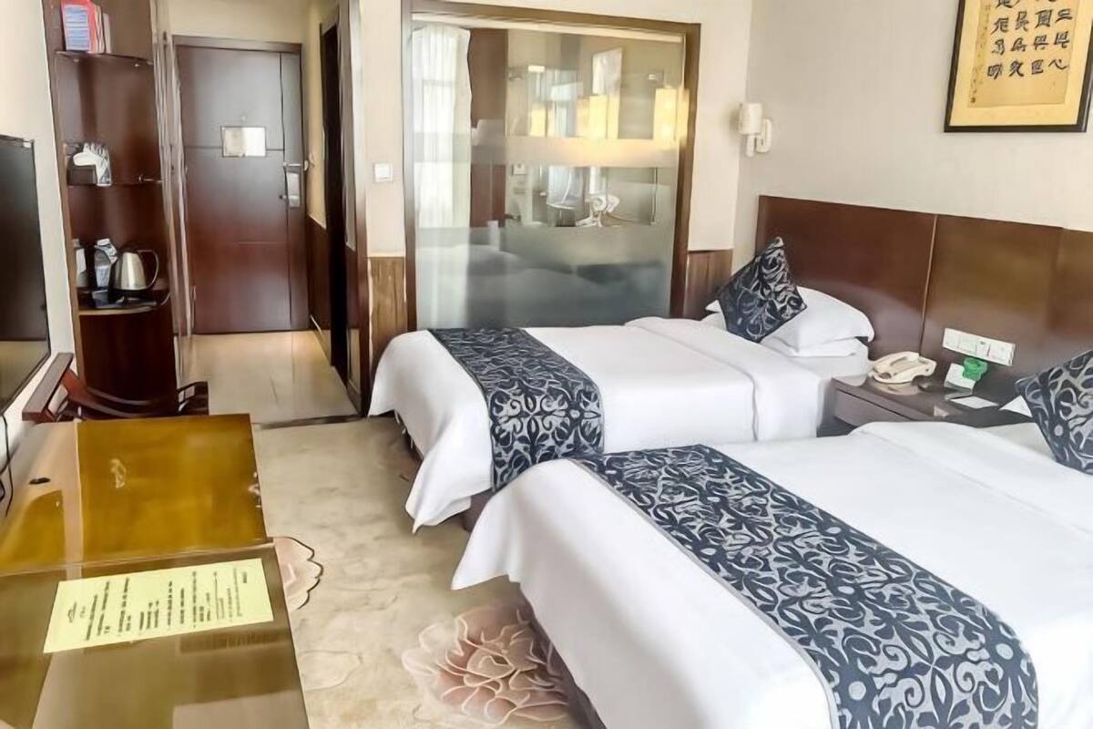 Une chambre d’hôtel avec deux lits, un bureau, une armoire et une salle de bain visible à travers une porte en verre.