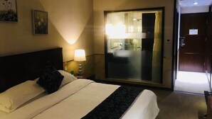 Une chambre d’hôtel avec un lit, une table de chevet avec une lampe, un grand miroir et une porte coulissante donnant accès à la salle de bain.