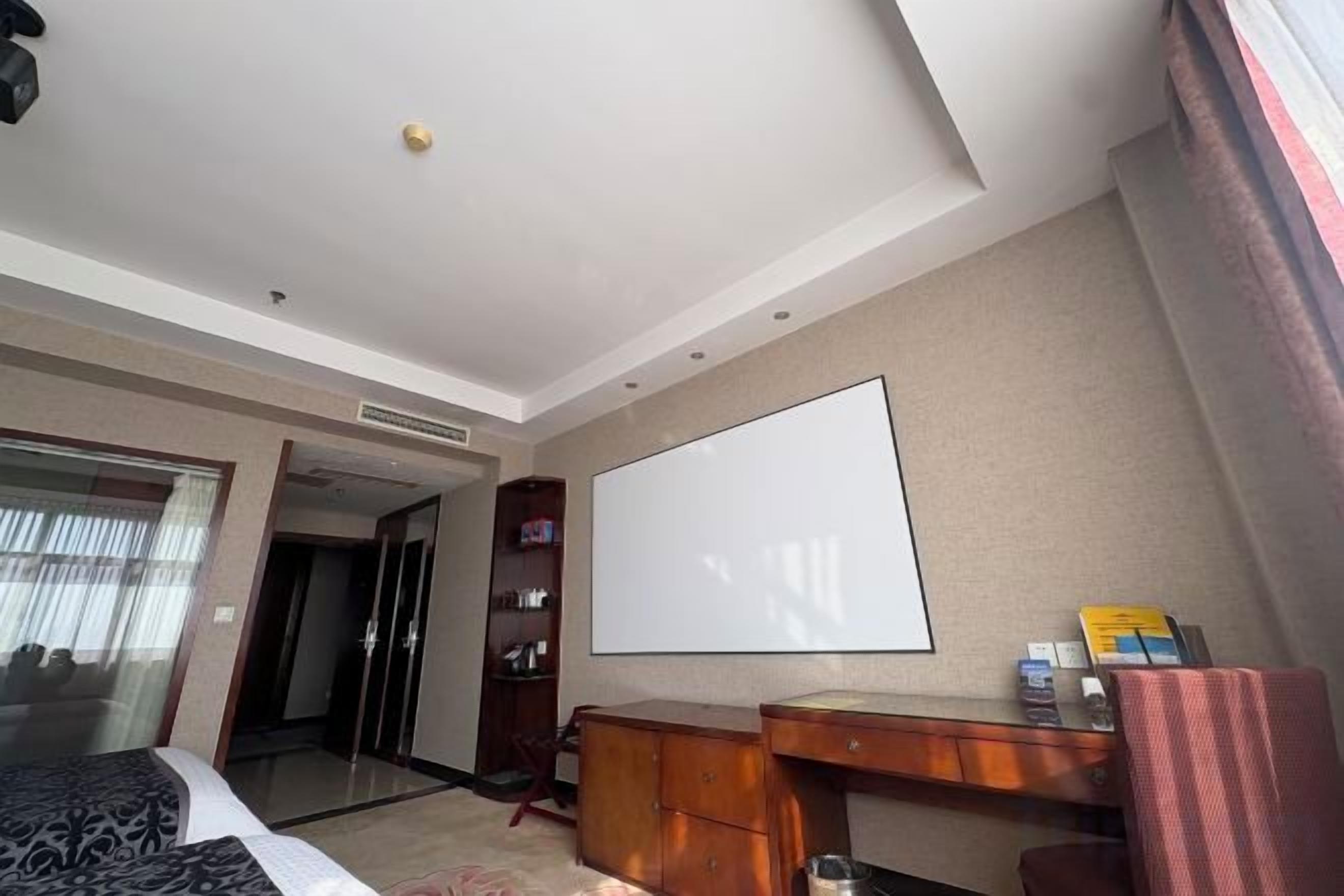 A hotel room with a bed, a desk, a flat-screen TV, a wardrobe, and a door leading to another room.