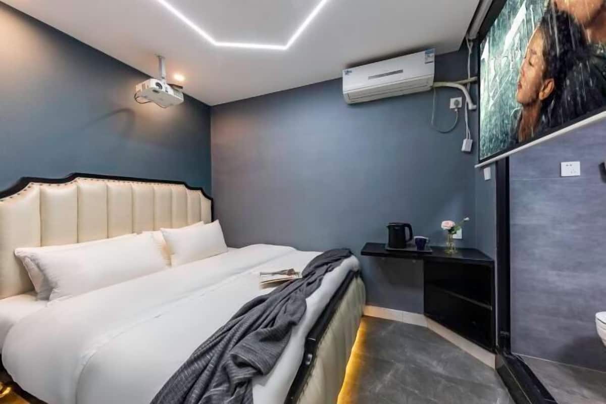 A modern hotel room with a bed, a bedside table, an air conditioning unit, and a television mounted on the wall.