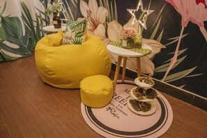 A room with a yellow bean bag chair, a small round table with a decorative item, and a wall with tropical wallpaper. - Jihe Light Luxury Art Hotel（Wuyi Square Station） (Changsha)
