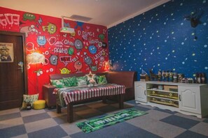 A room with a checkered floor, a bed with a striped blanket, a bookshelf, and a wall with various doodles and text.