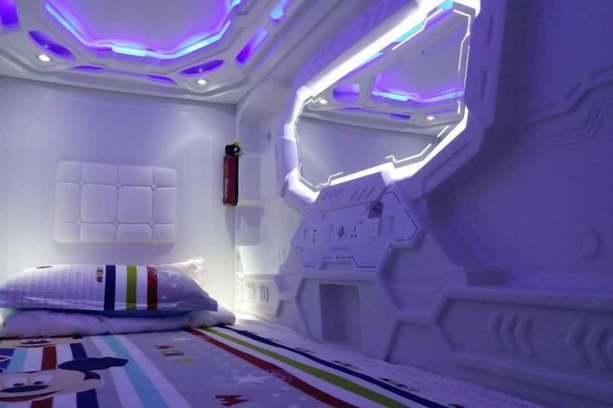 A room with a bed, a pillow, a wall-mounted control panel, and a ceiling with a geometric design.