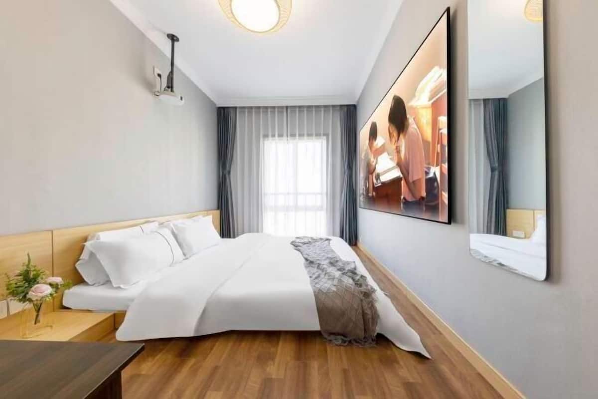 A hotel room with a bed, a bedside table, a mirror, and a window with curtains.