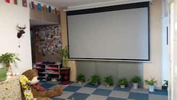 Een kamer met een groot projectiescherm, een teddybeer en verschillende potplanten.