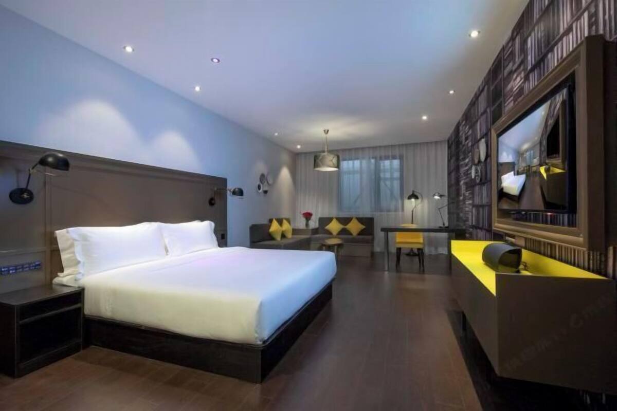 A hotel room with a large bed, a desk, a sofa, and a TV.
