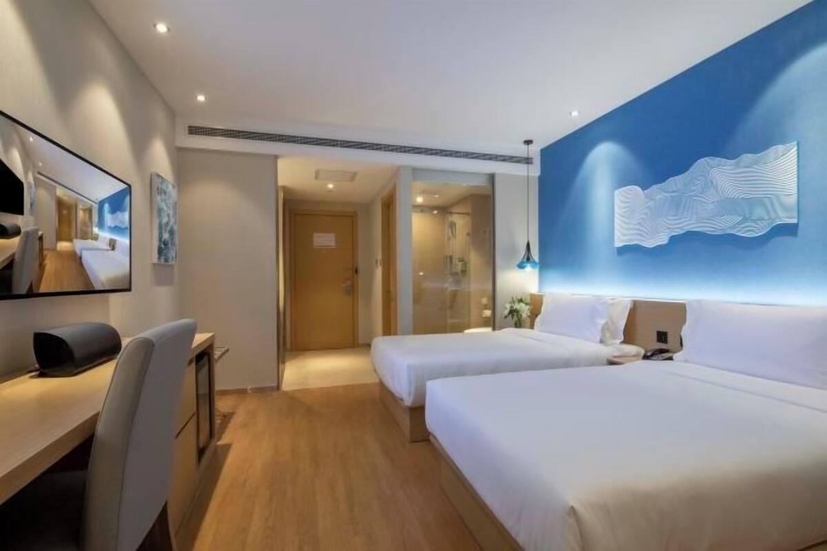 A hotel room with two beds, a desk, a chair, a mirror, and a wall-mounted artwork.