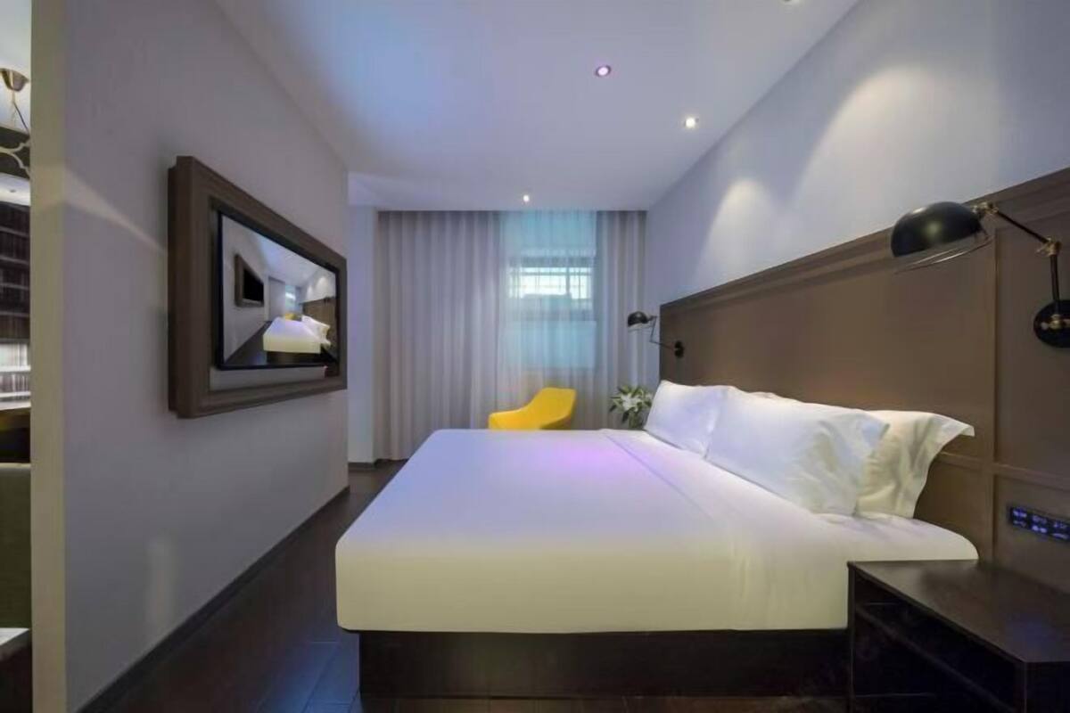 A hotel room with a bed, a chair, a TV, and a nightstand.