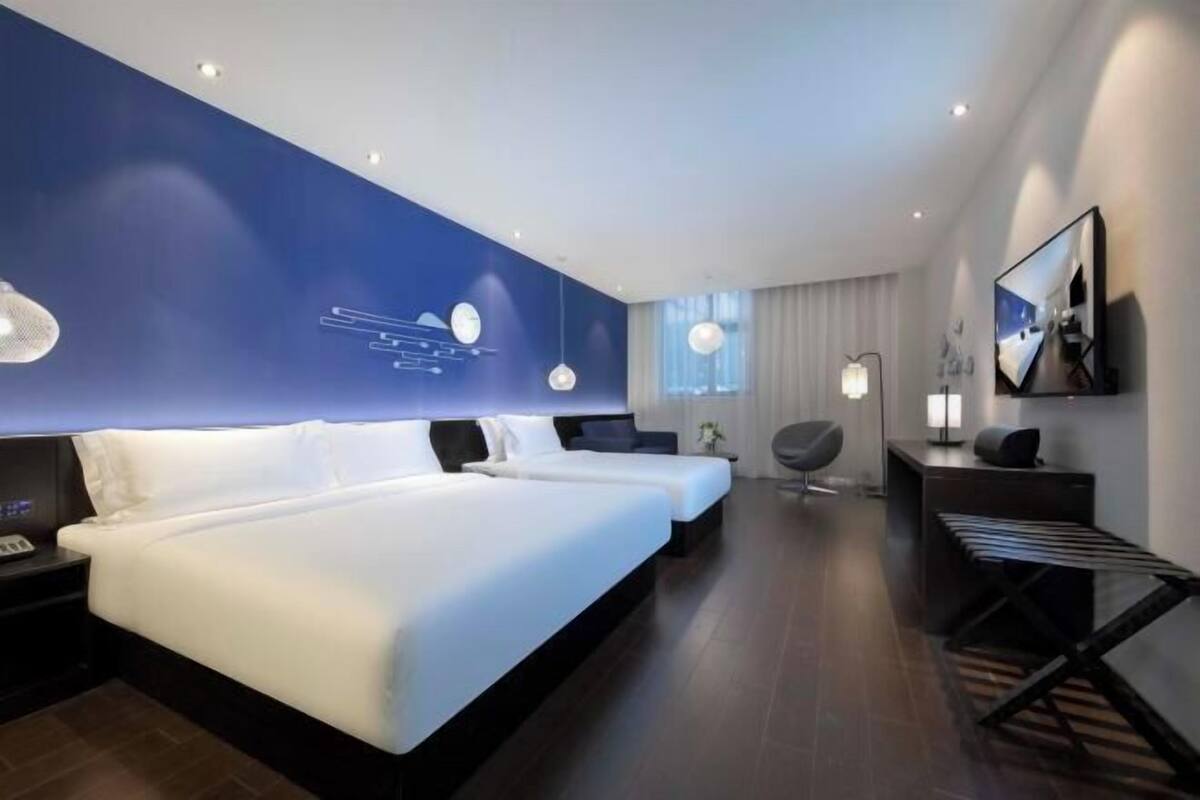 A modern hotel room with two beds, a desk, a chair, and a TV.