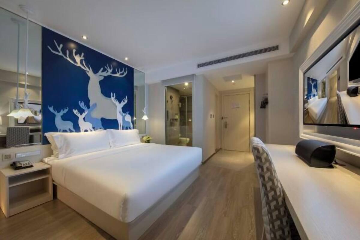 A modern hotel room with a large bed, a mirror, a nightstand, and a wall with a deer mural.
