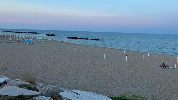 Una playa con sombrillas, sillas reclinables y un litoral rocoso.