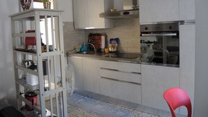 Una cocina con armarios blancos, una campana extractora de acero inoxidable, un lavamanos y una silla roja.