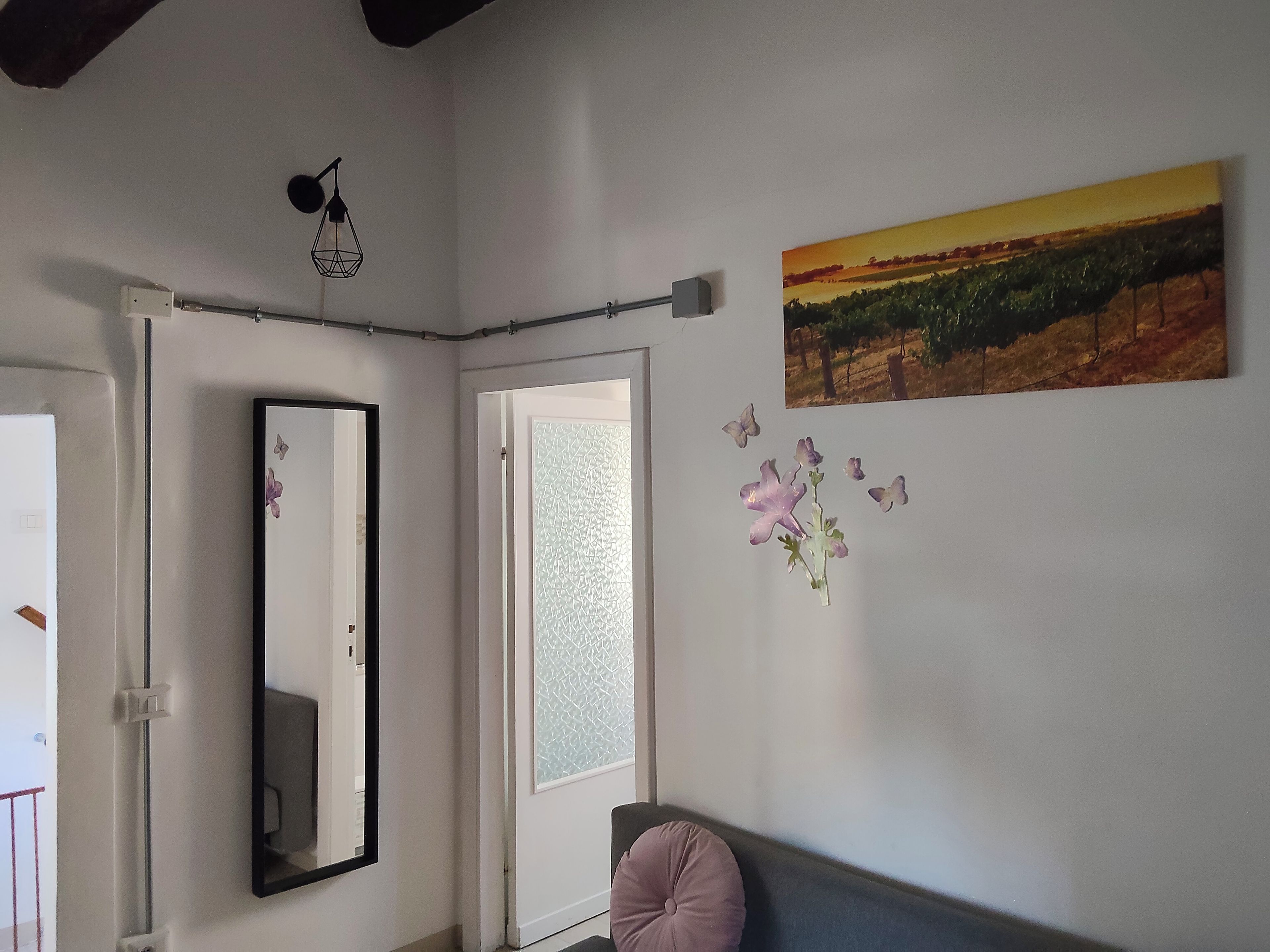 Una habitación con espejo, ventana, un cuadro y una lámpara en la pared.