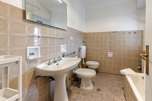 A bathroom with a sink, bidet, toilet, and a glass shelf.